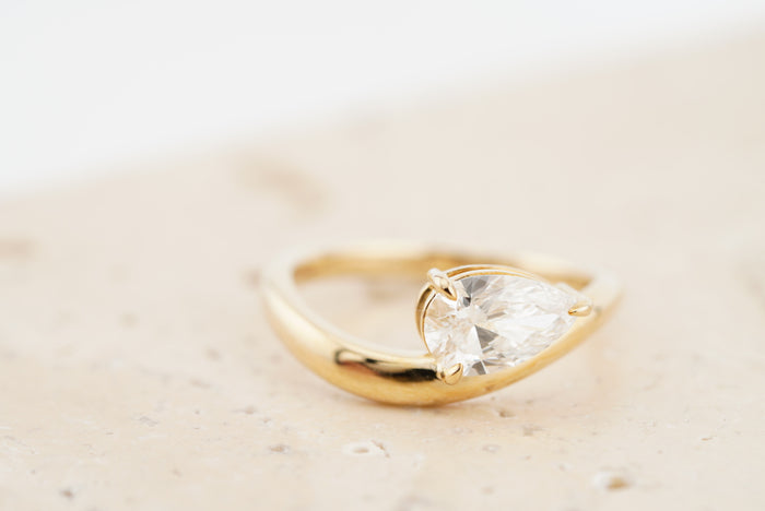 Wave Ring in 10K yellow gold with a pear-cut lab-grown diamond, on travertine